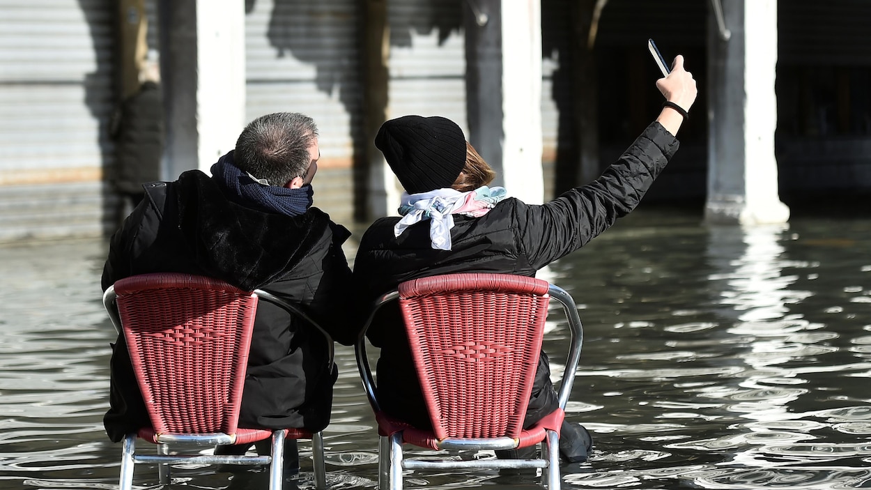 Un homme et une femme, les pieds dans l'eau, se prennent en photo.