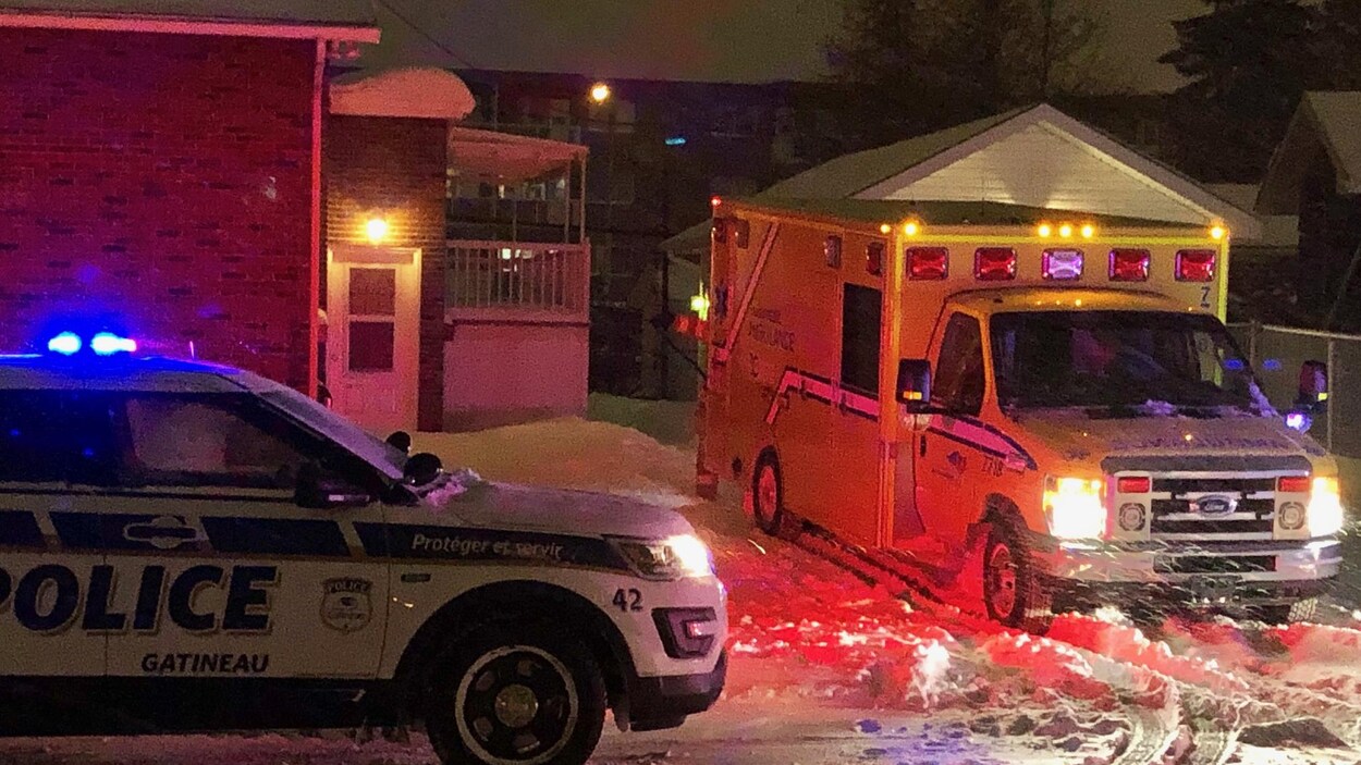Une ambulance et un véhicule du Service de police de la Ville de Gatineau stationnés près d'un immeuble en hiver, la nuit.