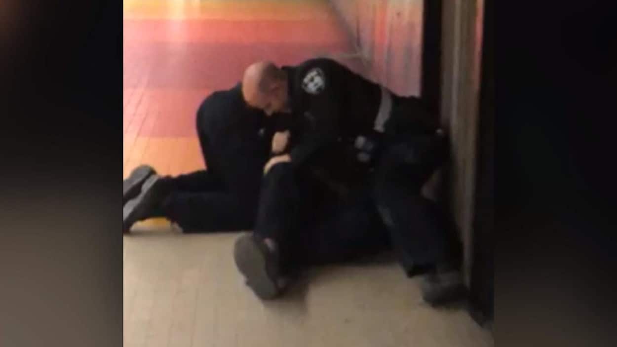 Deux inspecteurs tentent d'immobiliser un jeune homme au sol, dont on ne voit que les jambes et les pieds.