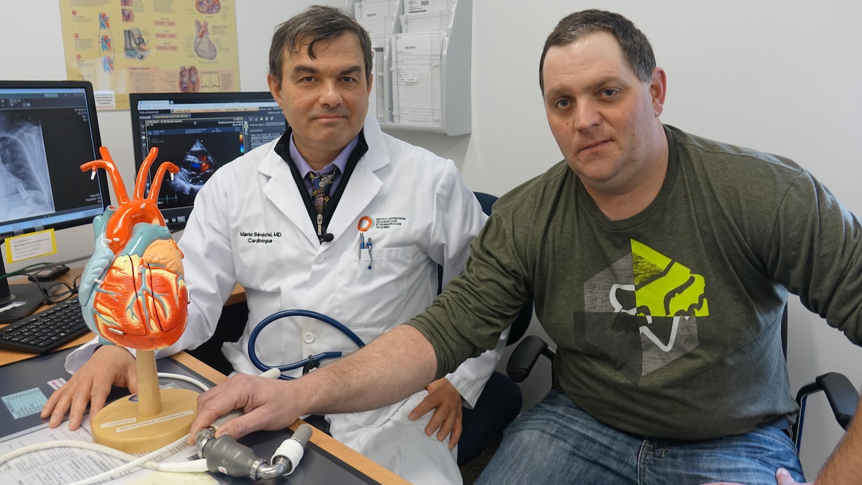 Le médecin Mario Sénéchal derrière un bureau avec son patient David Labrie, qui tient un coeur artificiel.
