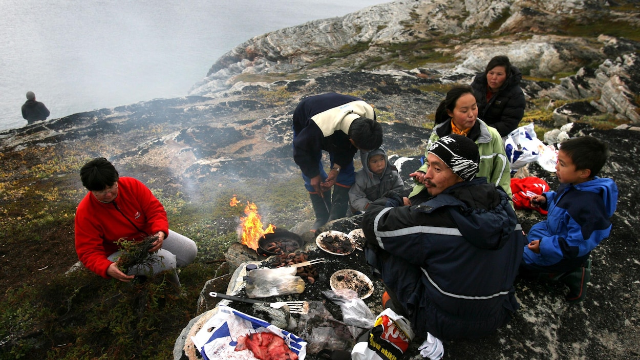 Une famille inuit mange à l'extérieur, sur une falaise au bord de la mer.