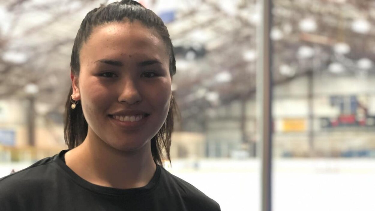 Une jeune femme regarde la caméra en souriant. Elle porte un chandail aux couleurs du championnat national de hockey autochtone.