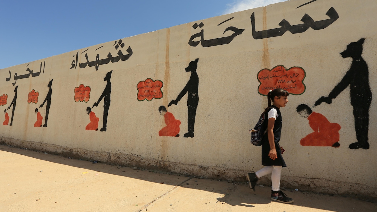 Elle passe devant une murale où des dessins montrent comment les membres du groupe armé État islamique exécutaient leurs prisonniers à Mossoul.