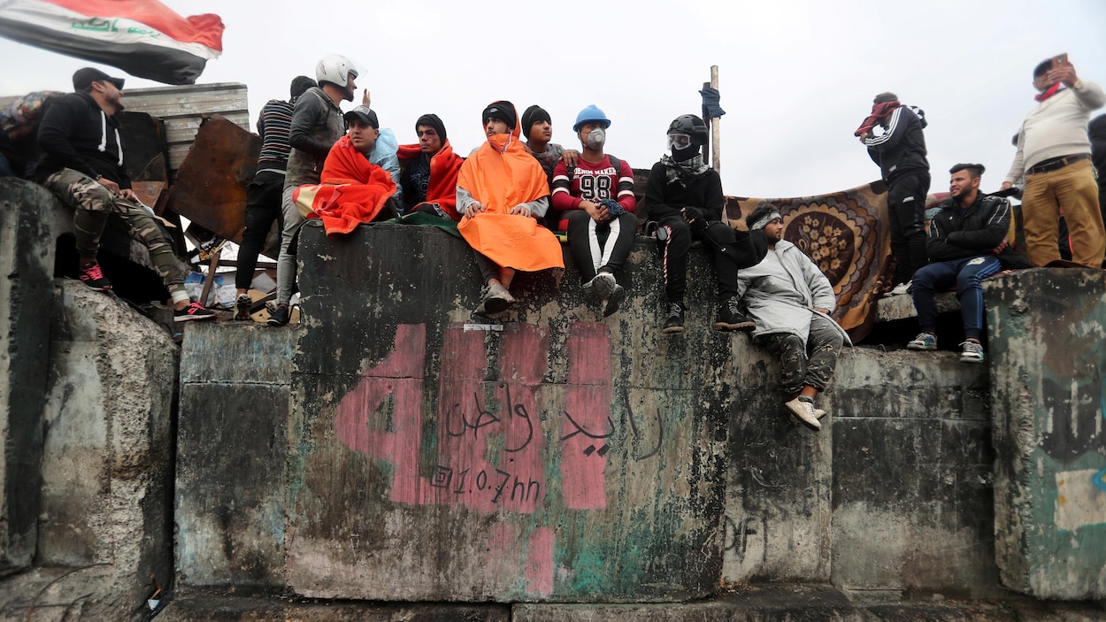 Des hommes assis et debout sur un mur