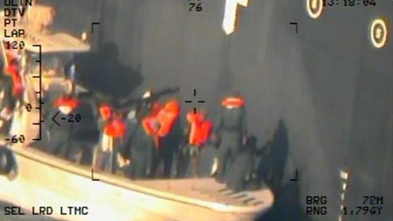 Des hommes portant des gilets sur une frégate près d'un bateau.
