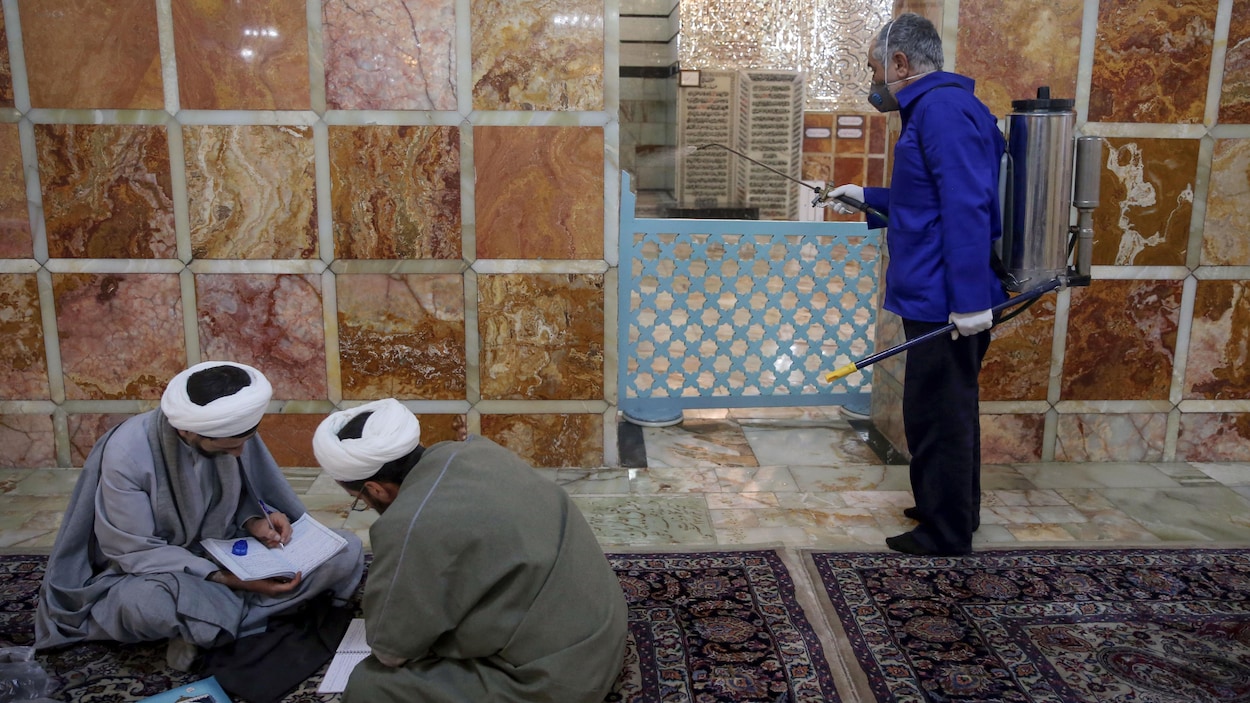 Un employé portant un masque désinfecte un sanctuaire. Deux religieux sont assis par terre et étudient.