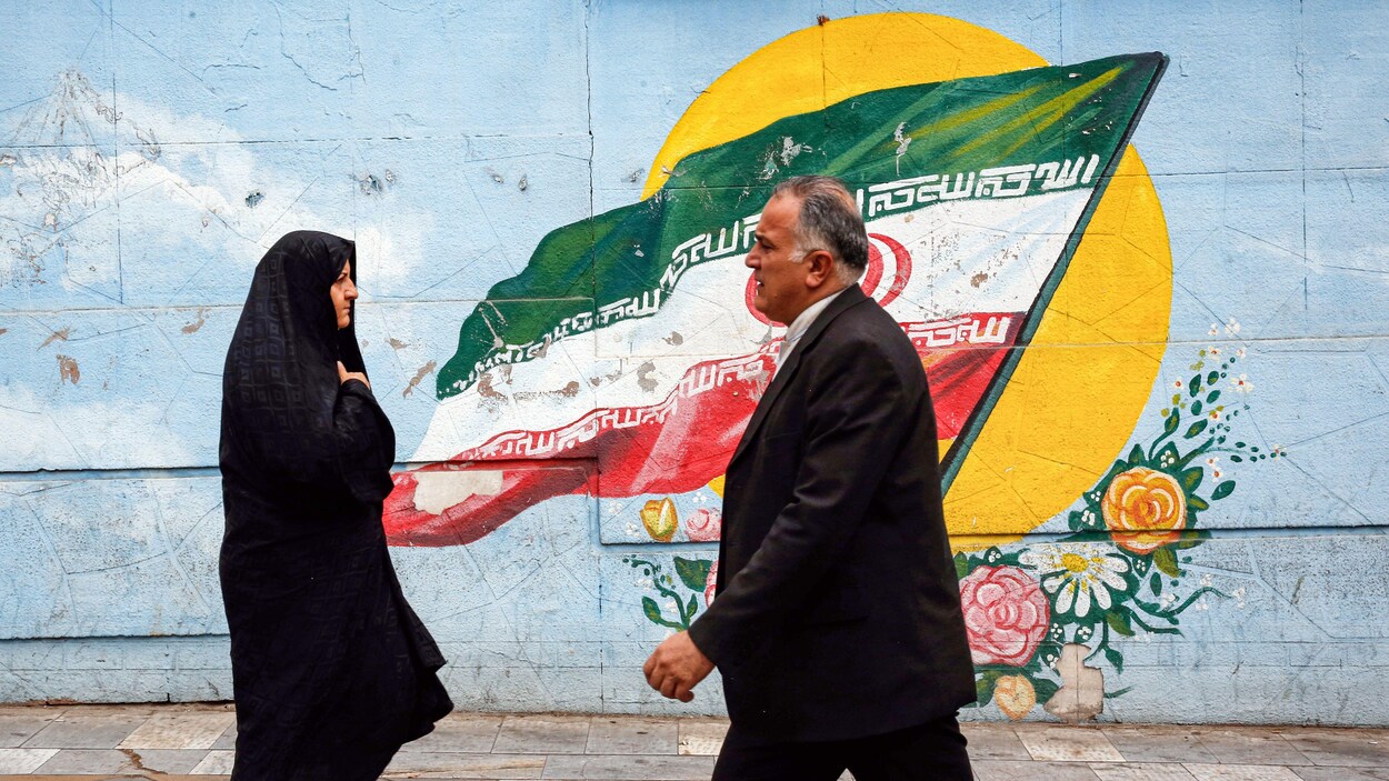 Des passants marchent devant une murale montrant un drapeau de l'Iran.