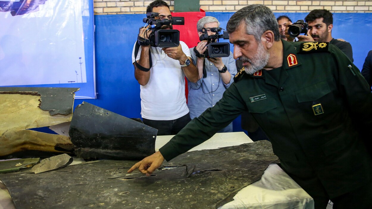 Le général Amir Ali Hajizadeh pointe un débris abîmé, des caméras se trouvent derrière lui.