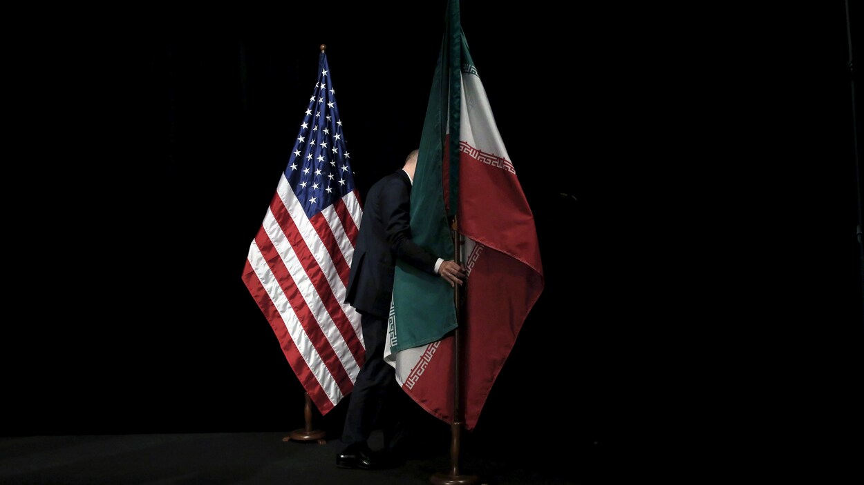 Un homme enlève les drapeaux des États-Unis et de l'Iran qui sont installés sur un socle après une séance photo.