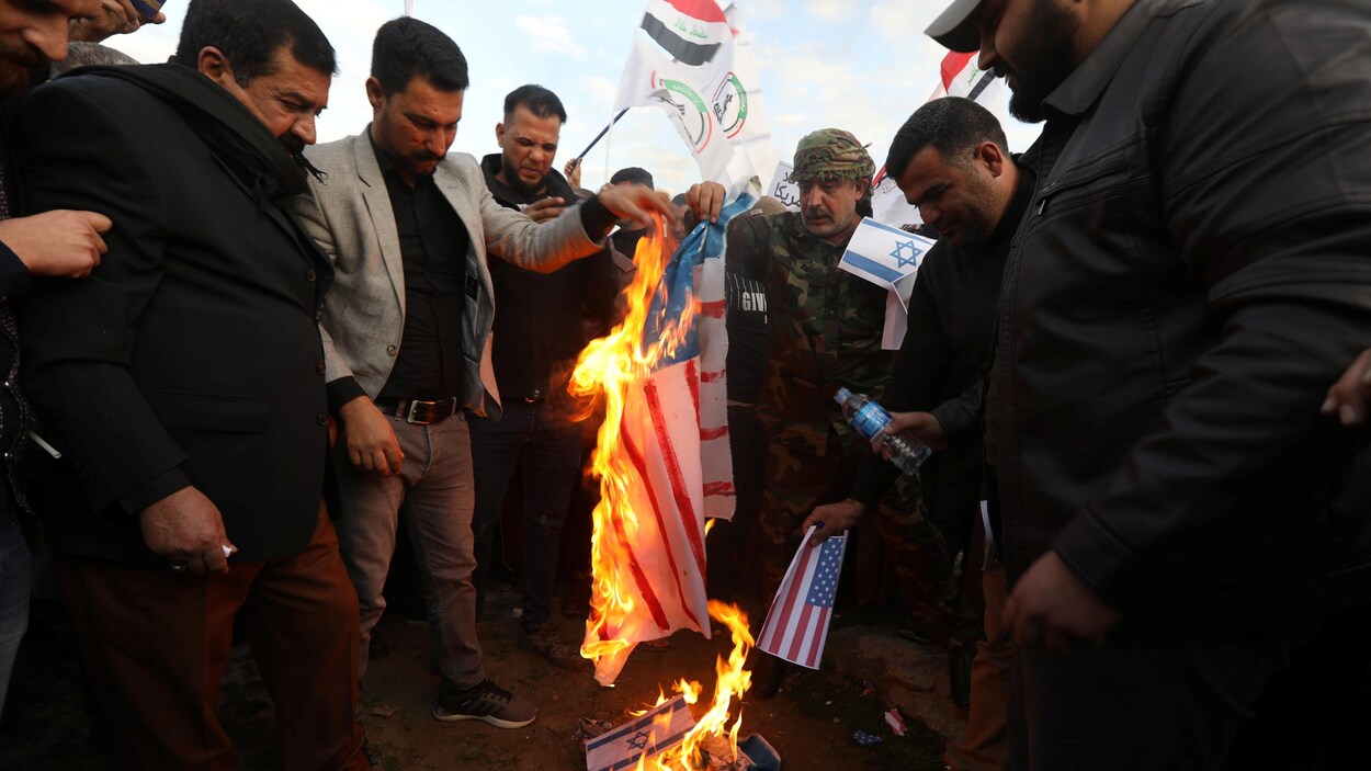 Des hommes rassemblés autour de drapeaux américains et israéliens qui brûlent.
