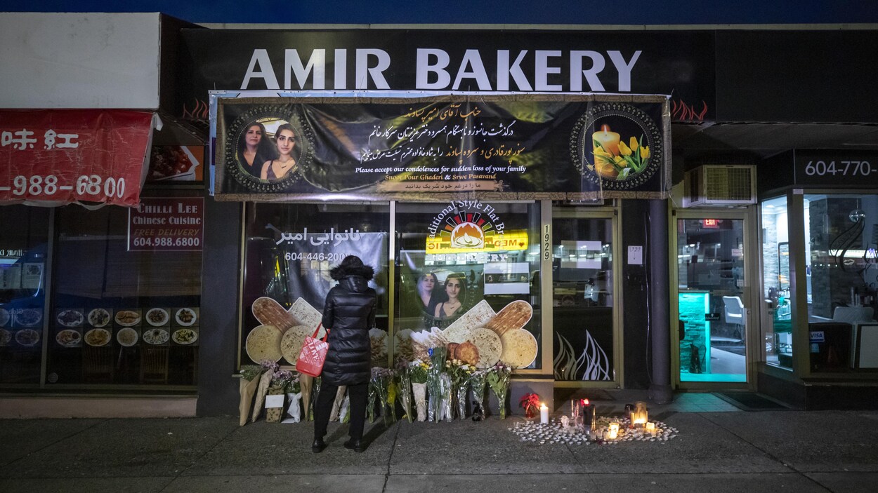 De nombreux bouquets de fleurs sont déposés au bas de la vitrine et des chandelles brûlent sur le trottoir devant la boulangerie Amir. Une passante se recueille devant ce mémorial improvisé.