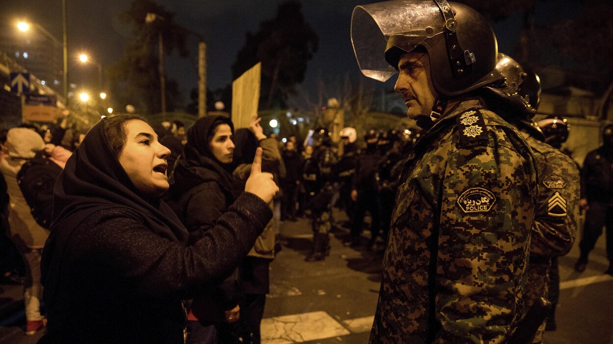 Une femme participant à une veillée aux chandelles en hommage aux victimes de l’écrasement de l’avion ukrainien parle à un policier près de l'Université Amri Kabir à Téhéran, en Iran.