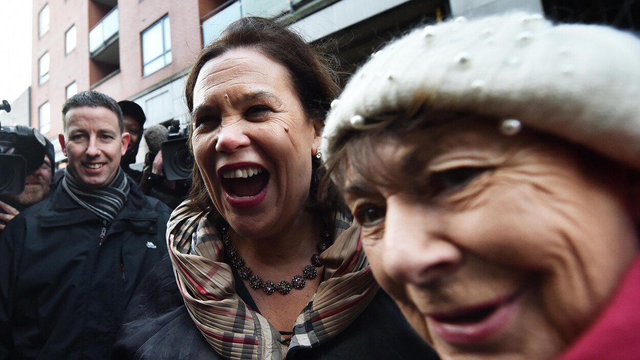 Deux femmes sourient à la caméra dans une mêlée publique.