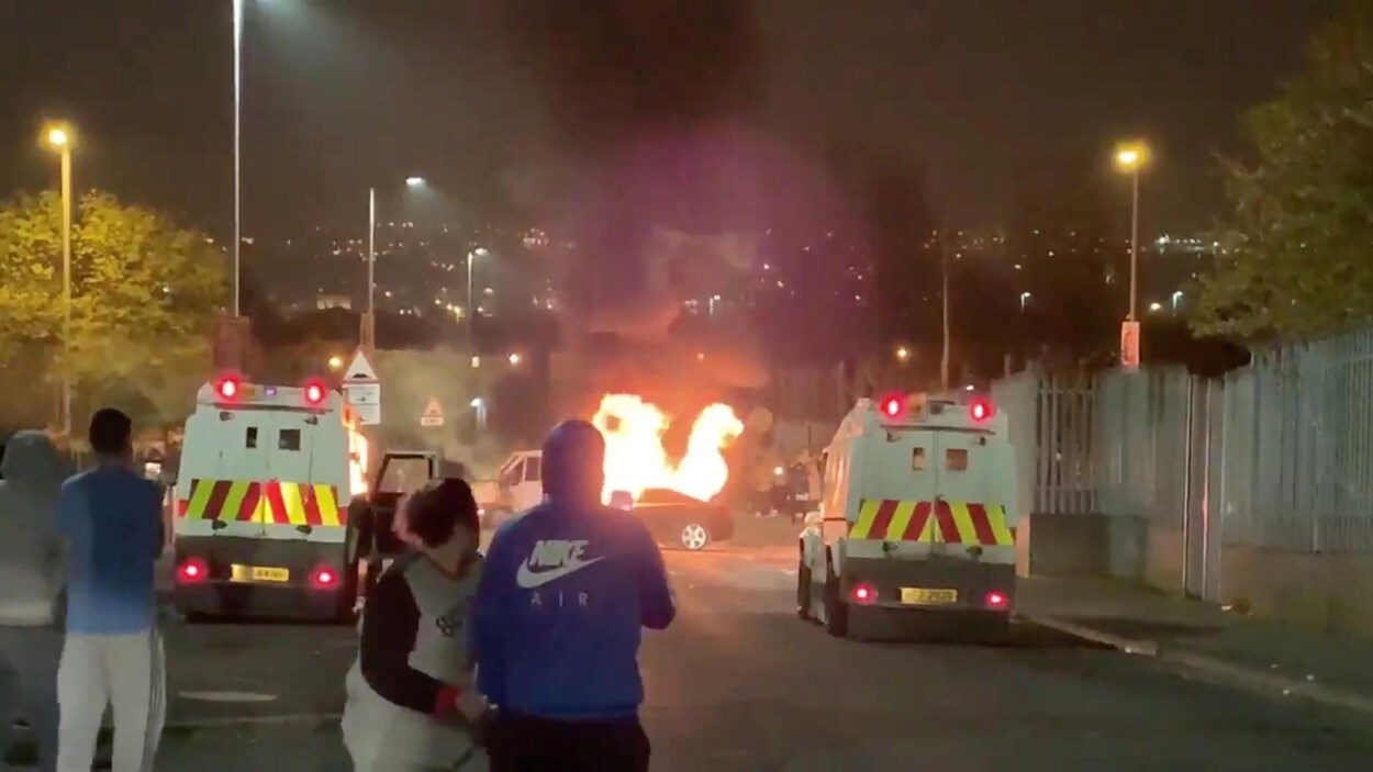 Des manifestants observent une voiture en feu.