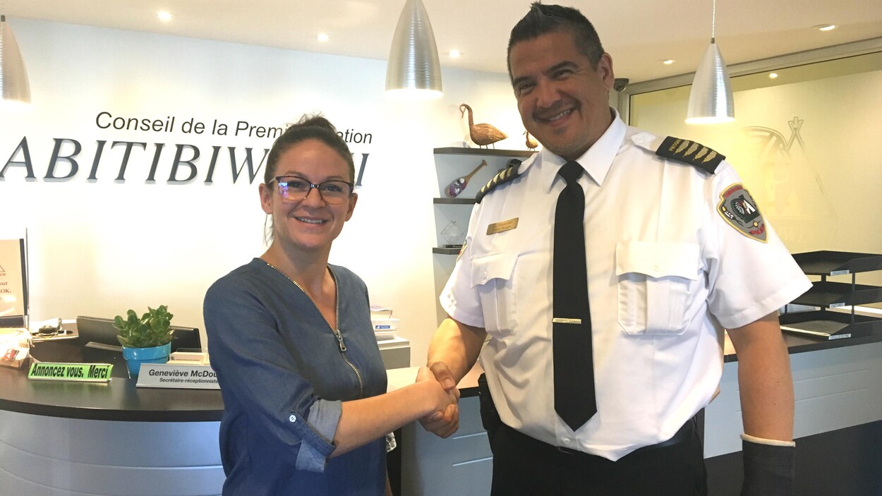 Une femme et un homme portant un uniforme de police se serrent la main, regardant la caméra.