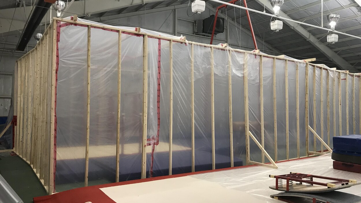 De grands plastiques sont tendus sur une structure de bois pour créer un espace scellé à côté des tapis de gymnastique.