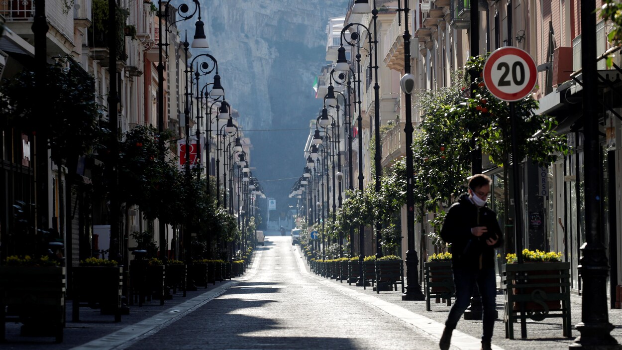 Un homme portant un masque marche dans une rue déserte.