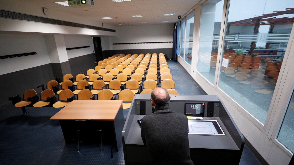 Un professeur est vu de dos devant une classe vide.