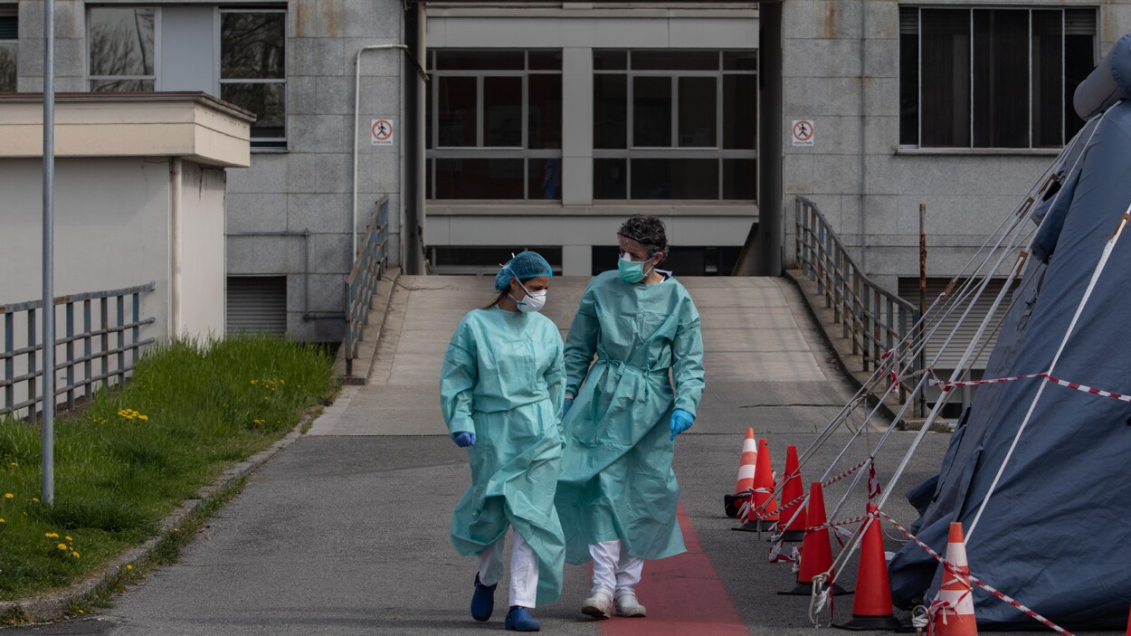 Deux infirmiers vêtus de tuniques et de masques sortent d'un hôpital.