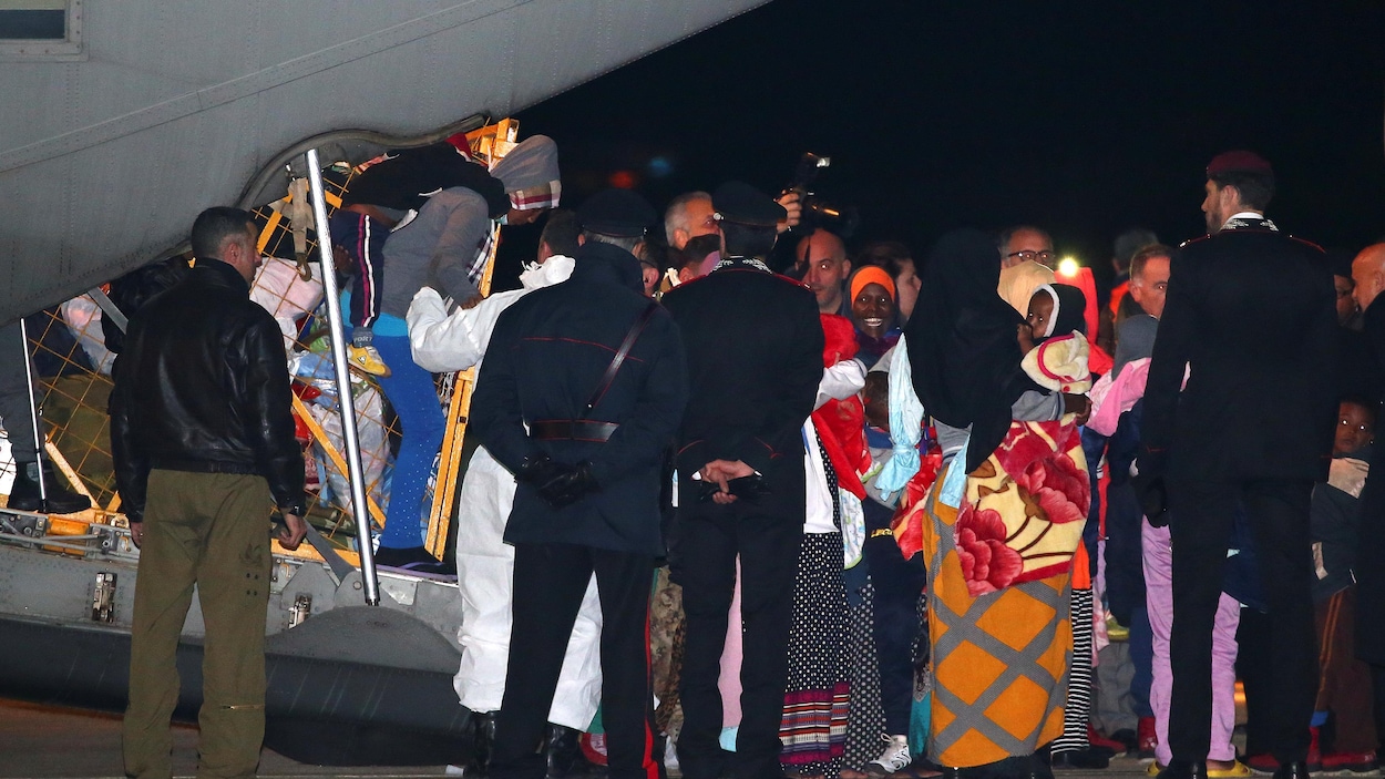 Des réfugiés sortent de la queue d'un avion cargo militaire devant le regard de policiers italiens. Des réfugiés sortent de la queue d'un avion cargo militaire devant le regard de policiers italiens.