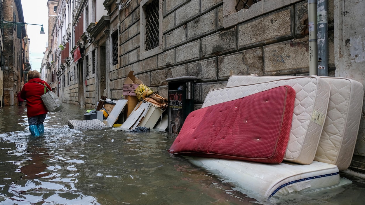 Une femme marche avec de l'eau pratiquement jusqu'aux genoux dans une rue inondée de Venise.