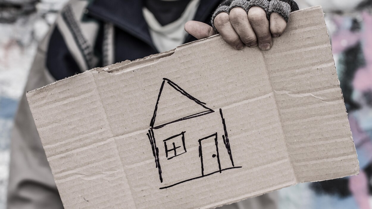 Un itinérant tiens une pancarte de carton avec une maison dessiné dessus. Un itinérant tiens une pancarte de carton avec une maison dessiné dessus.