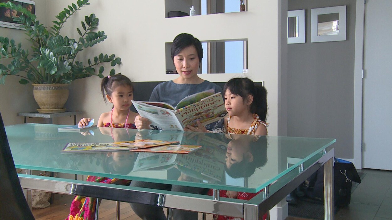 Une femme asiatique lit un livre à ses deux filles qui l'entourent dans une cuisine. Une femme asiatique lit un livre à ses deux filles qui l'entourent dans une cuisine.