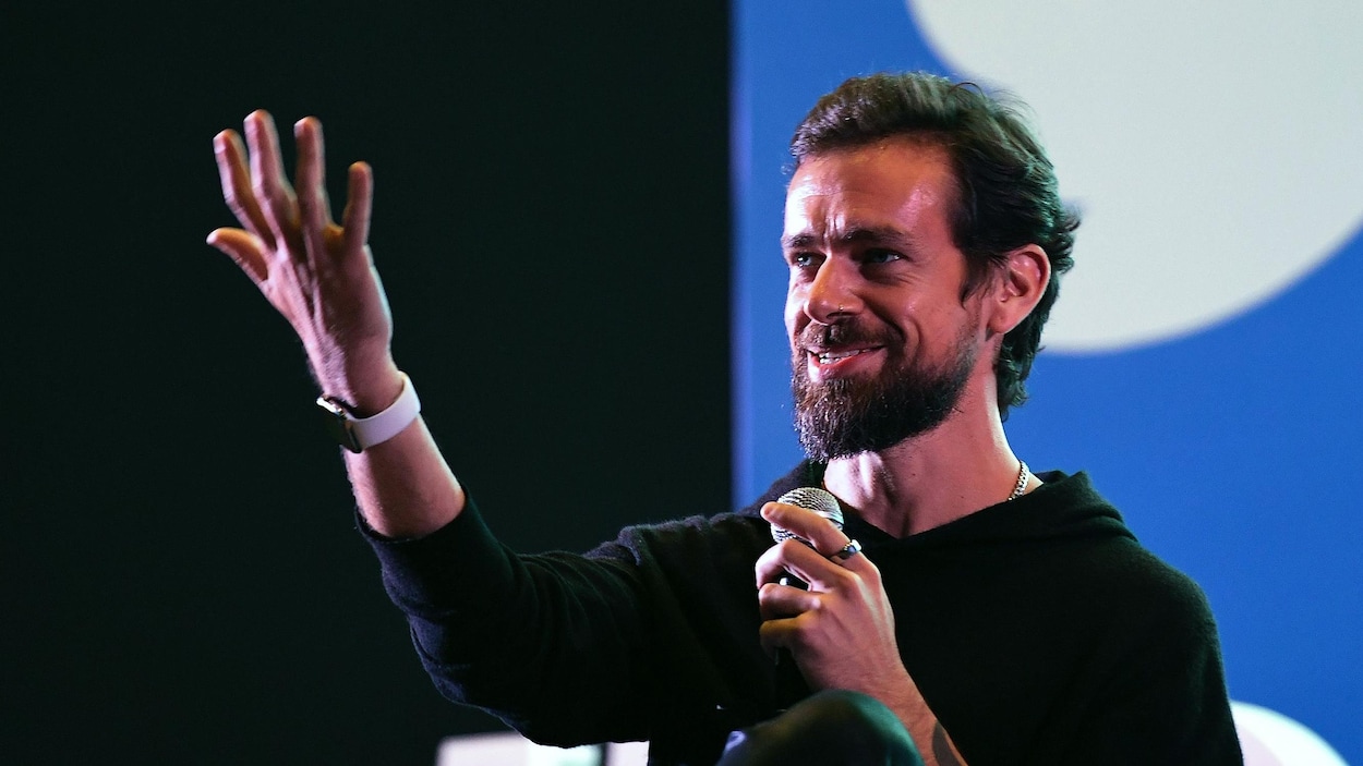 L'homme parle sur scène avec un micro lors d'une conférence. On aperçoit en arrière-plan le logo de Twitter.