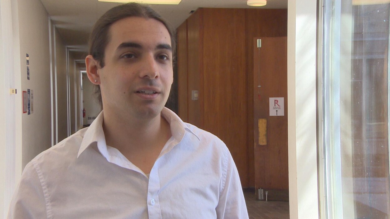Un homme en chemise blanche debout dans un couloir.