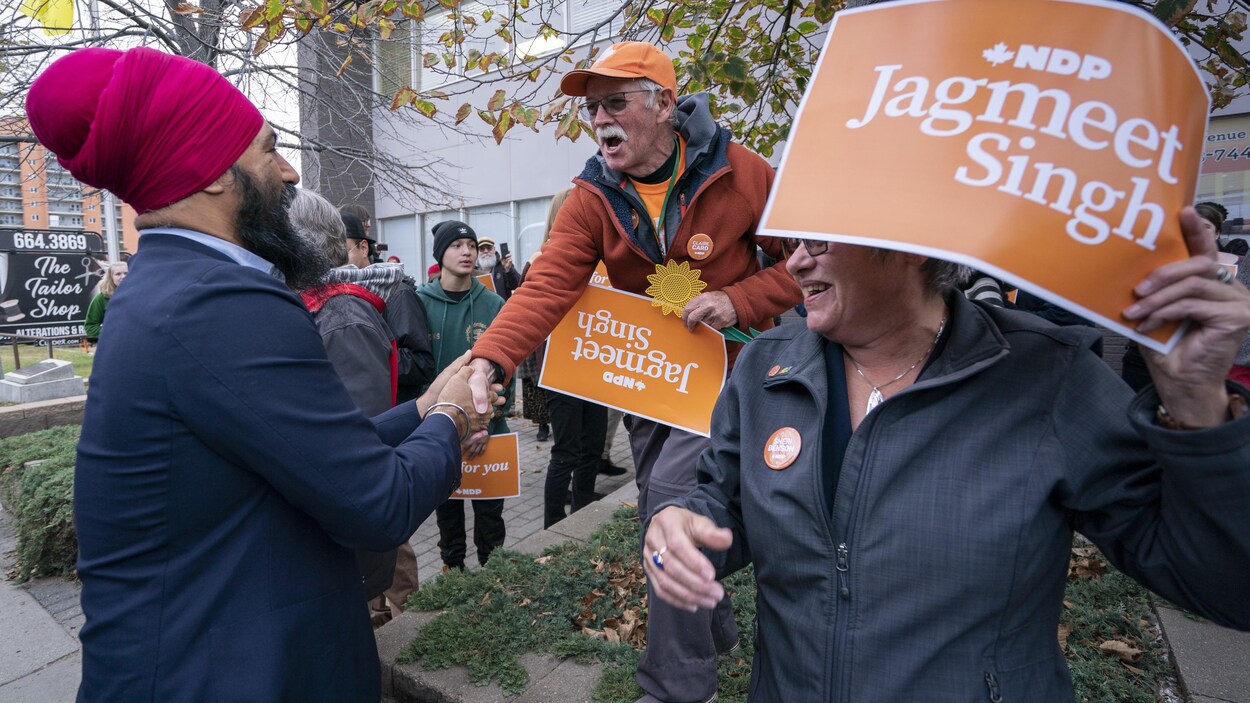 Jagmeet Singh serre la main d'un partisan tenant une affiche orange à son nom.