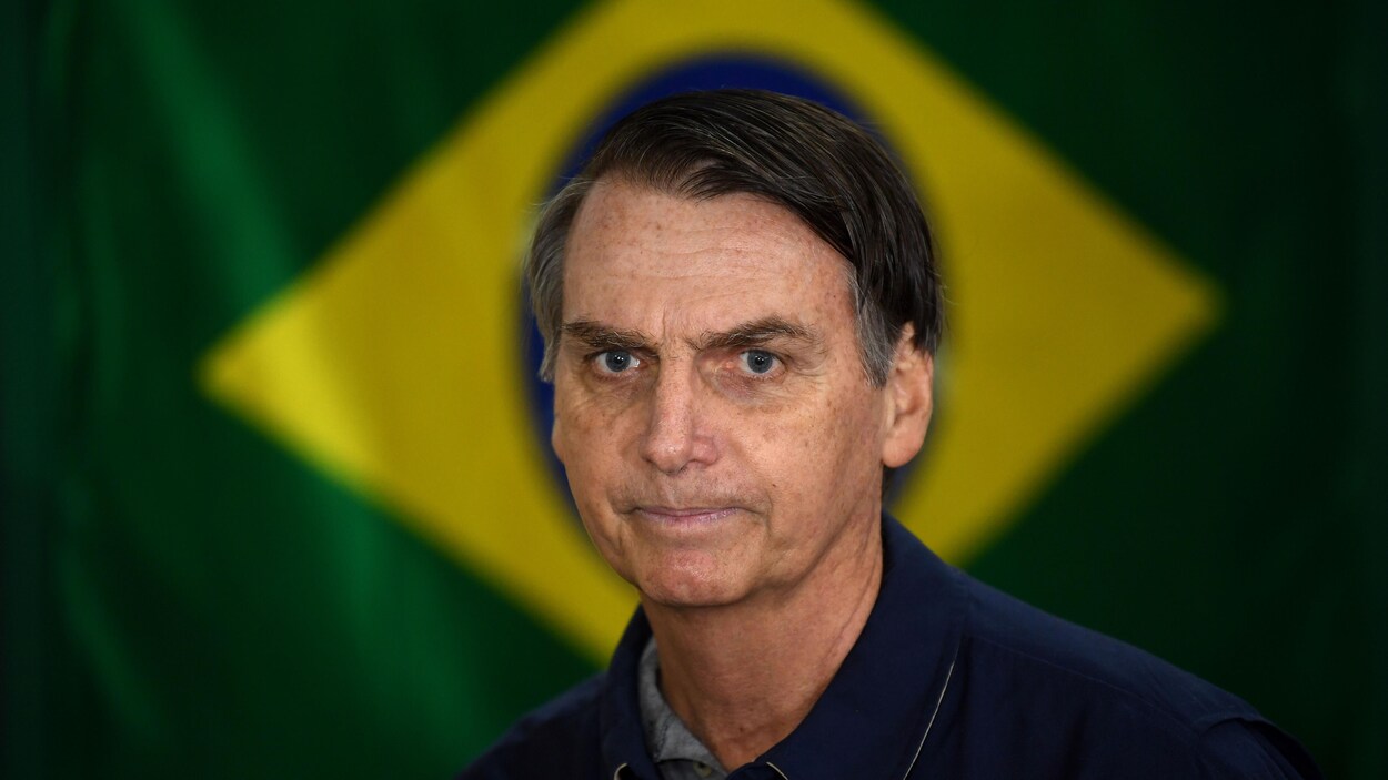 Jair Bolsonaro se tient devant un drapeau brésilien.