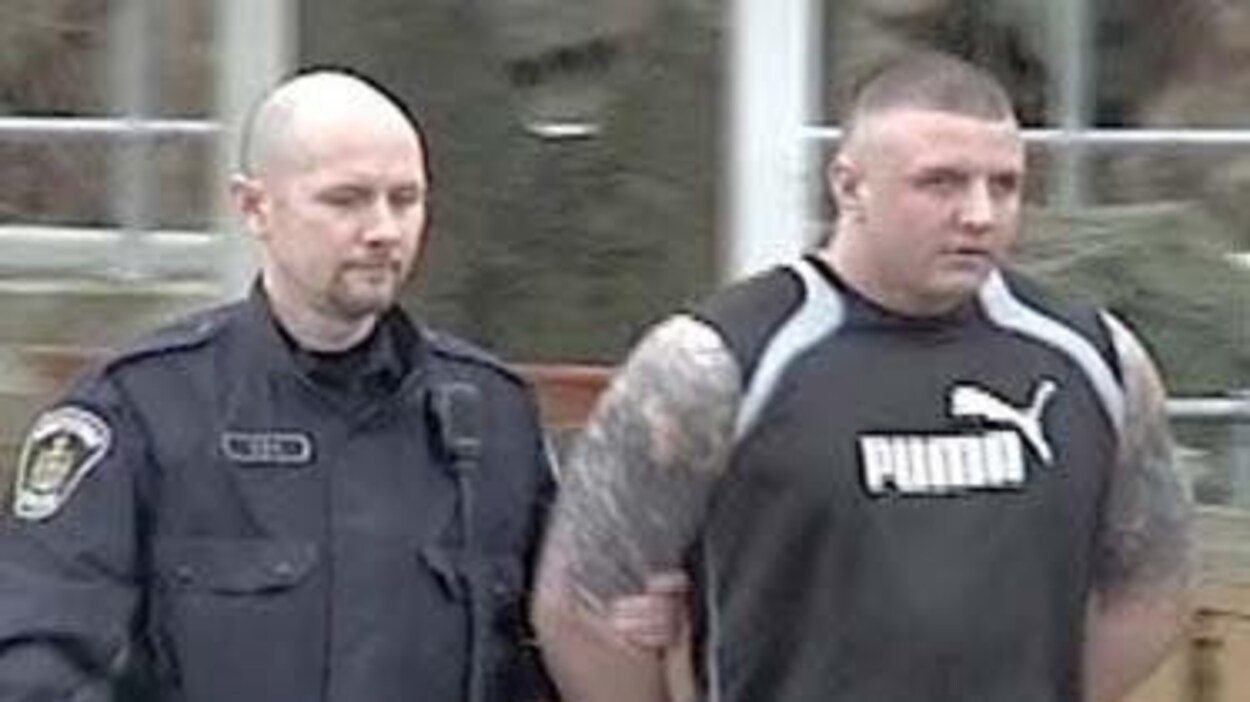 Jamie Bacon menotté est accompagné par un policier Jamie Bacon menotté est accompagné par un policier