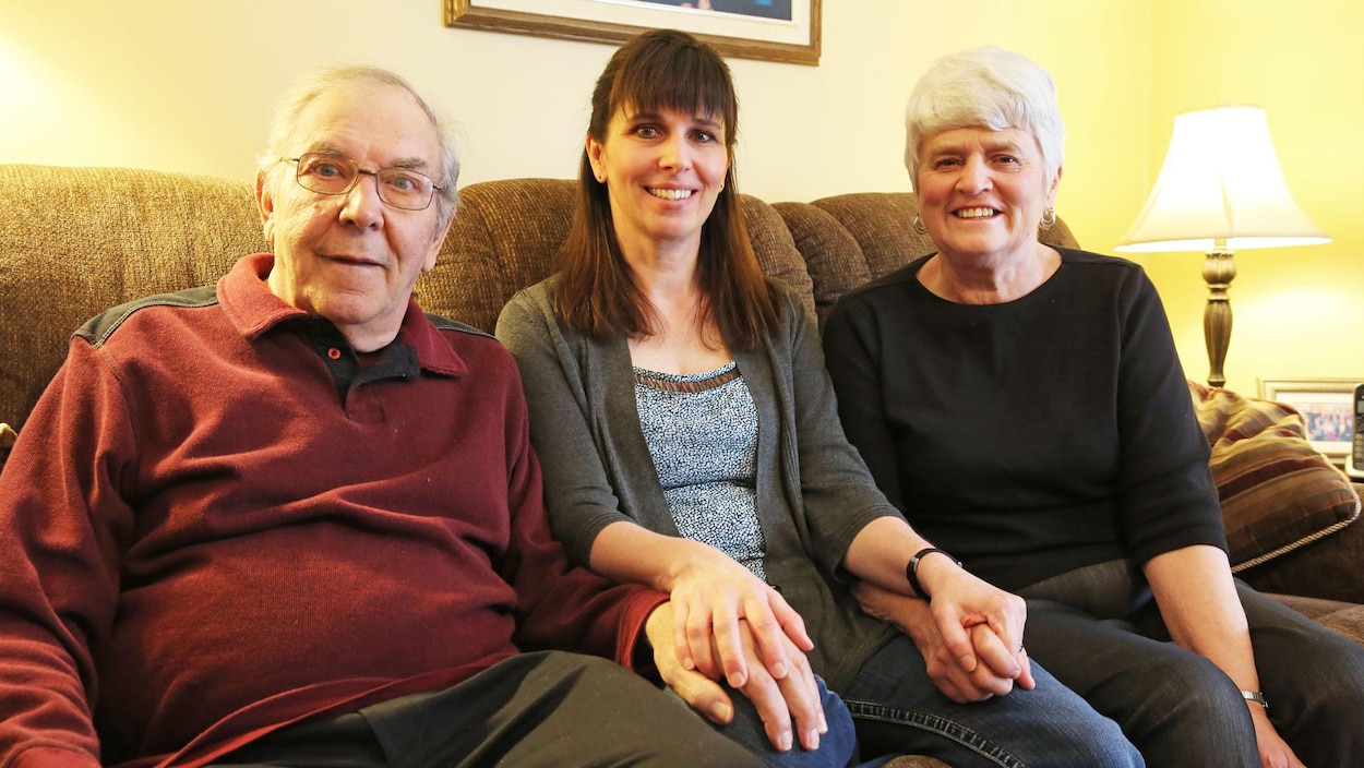 Les trois personnes assises sur le canapé de leur maison.