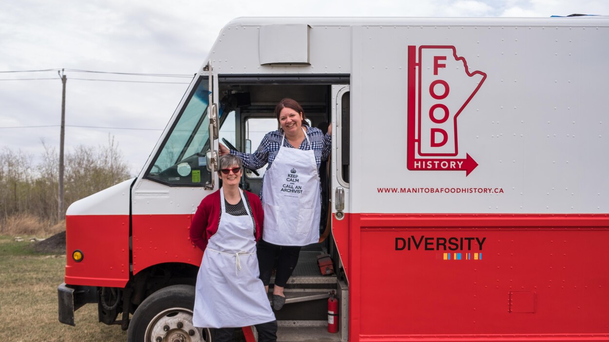 Deux femmes posent devant un camion restaurant repeint en blanc et rouge et sur lequel on lit Manitoba Food History. Deux femmes posent devant un camion restaurant repeint en blanc et rouge et sur lequel on lit Manitoba Food History.