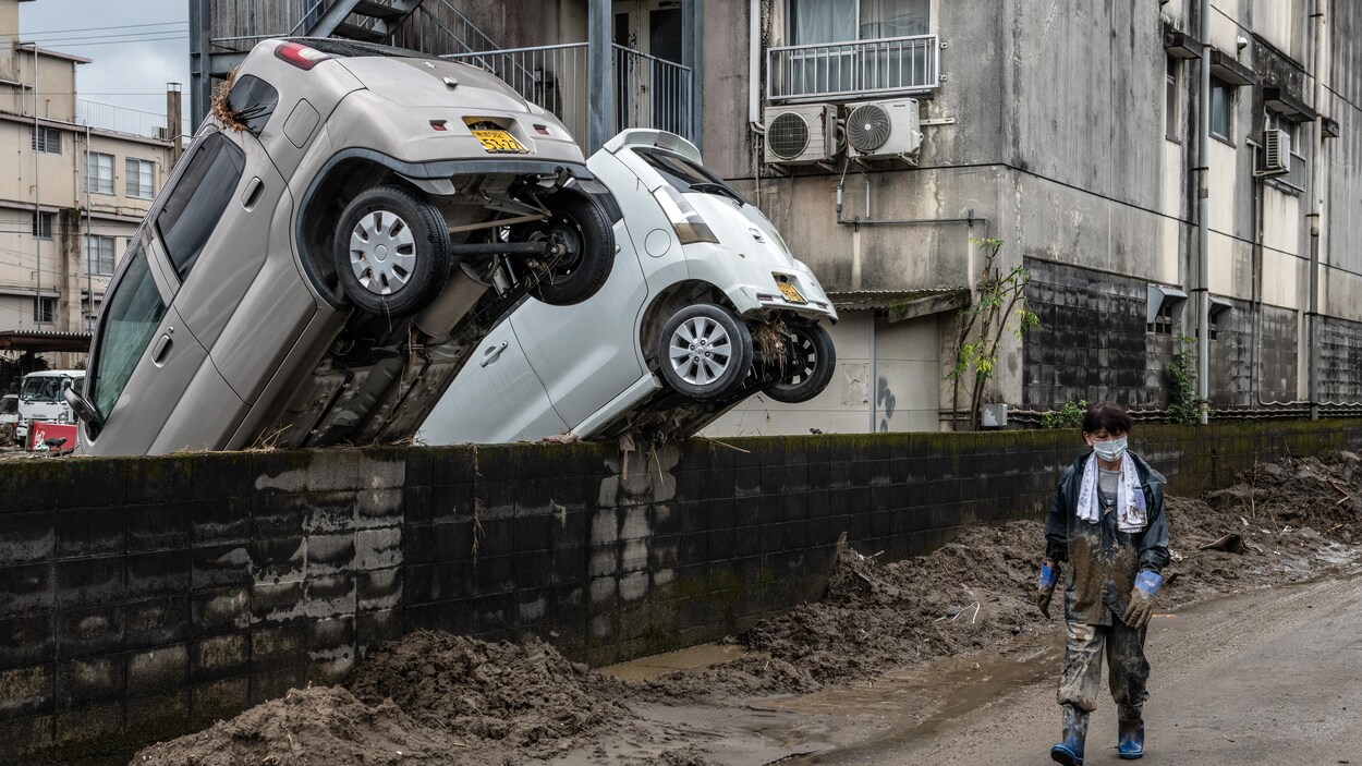 Une femme passe devant des voitures bloquées contre un mur, où les traces de boue témoignent de la force des pluies qui ont fait déborder la rivière Kuma et inondé la région.