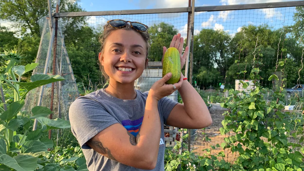 Madison Pierce pose pour la caméra dans un jardin. Elle a un concombre dans les mains qu'elle montre fièrement.