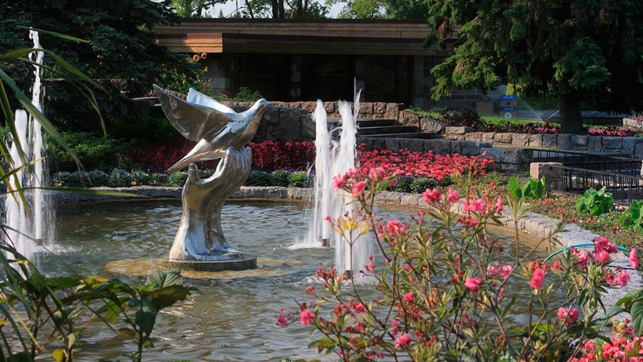 Une sculpture dans une fontaine entourée de fleurs.
