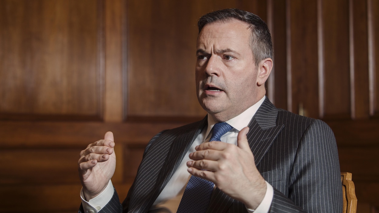 Jason Kenney répond aux questions d'un journaliste lors d'une entrevue. Il est assis sur une chaise et porte un complet.