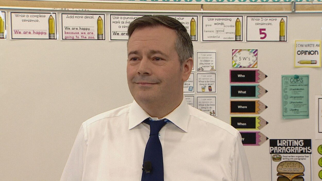 Jason Kenney sourit devant un tableau dans une classe.