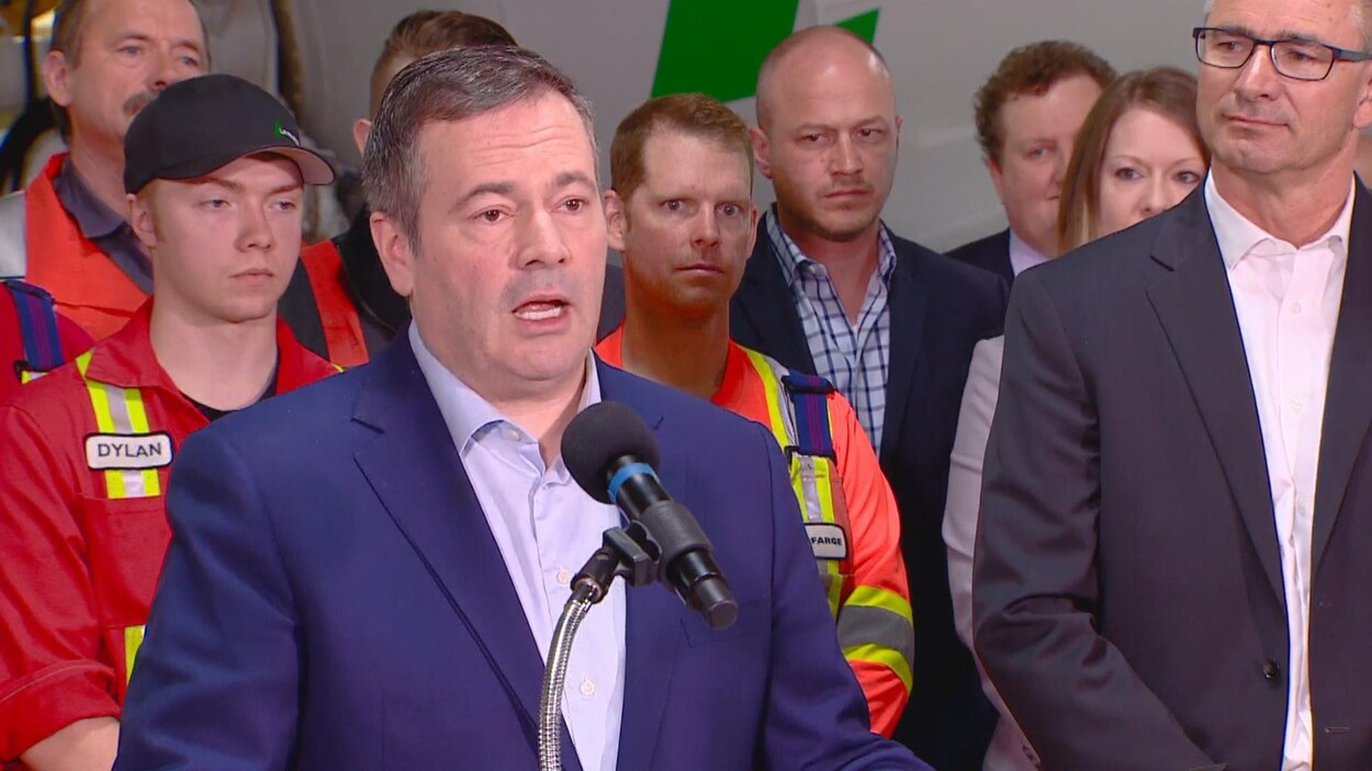 Jason Kenney parle à un micro devant des travailleurs de la compagnie Lafarge.