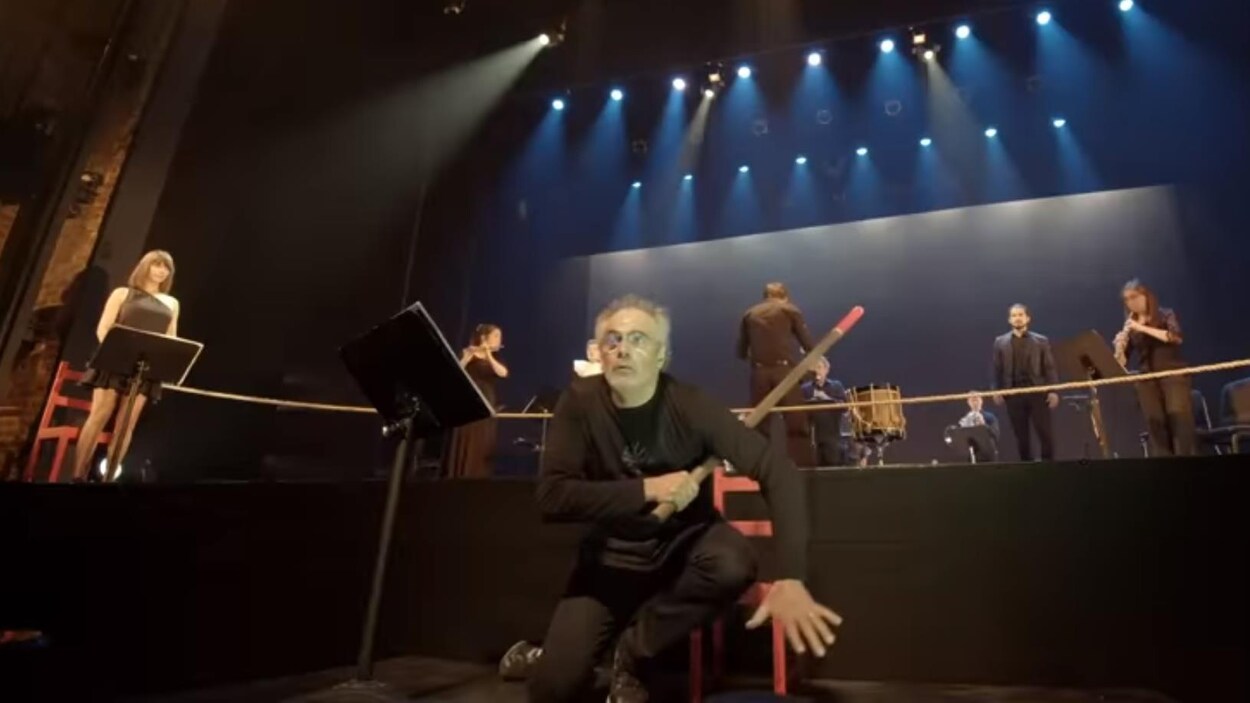 Un homme vêtu de noir tient un bâton et est accroupi devant une scène de théâtre.