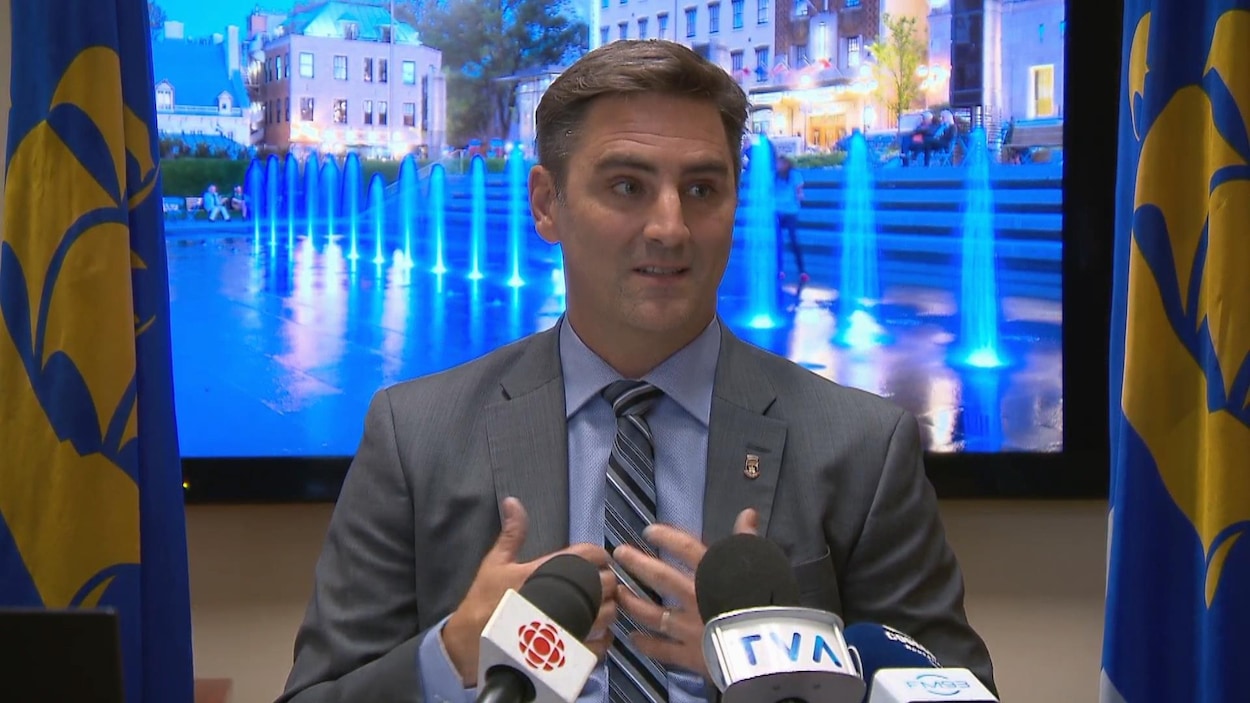 Jean-François Gosselin devant un écran et deux drapeaux de la Ville.