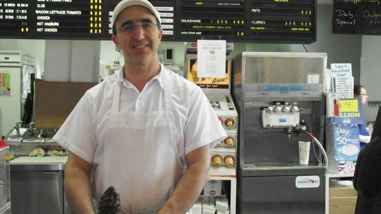 Jean LeBlanc derrière le comptoir de son commerce, un cornet de crème glacée au chocolat dans la main.