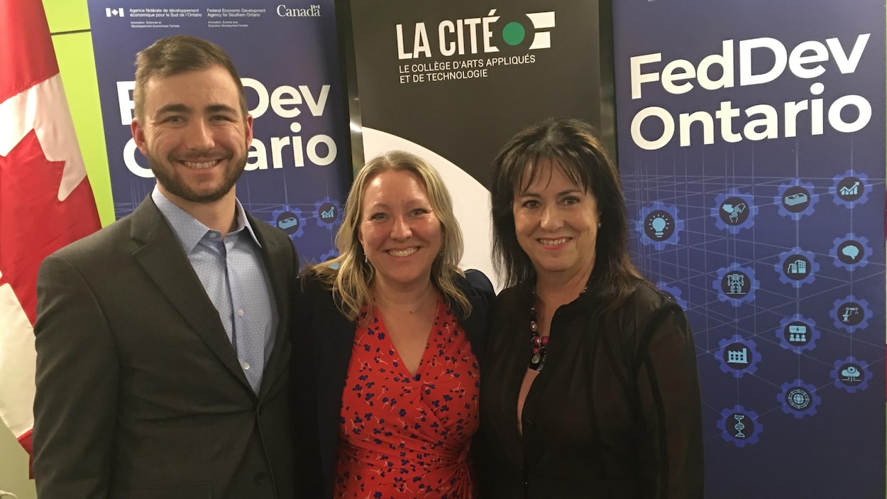 Jean-Philippe Héroux, entrepreneur (à gauche), Mona Fortier, députée fédérale d’Ottawa-Vanier (au milieu) et Lise Bourgeois, présidente-directrice générale de La Cité, sourient devant des panneaux FedDev et un drapeau canadien.