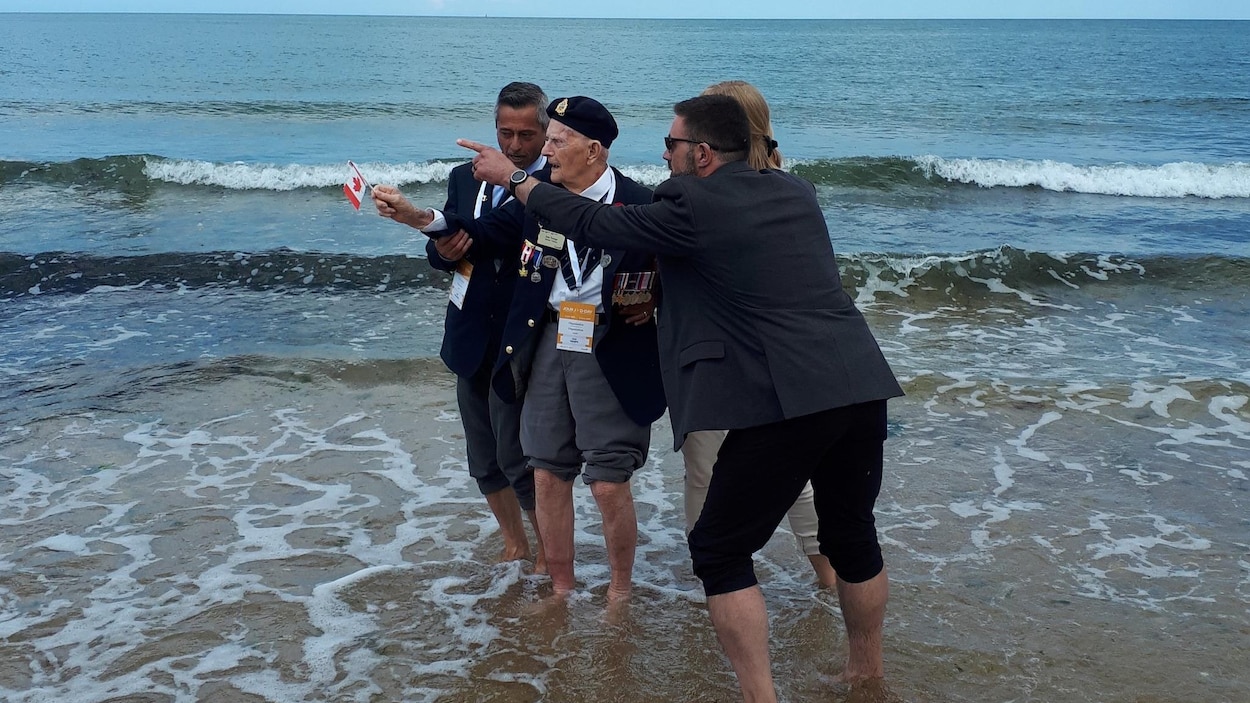 L'ancien combattant Jean Trempe, entouré de quelques personnes, a les pieds dans l'eau à la plage Juno.