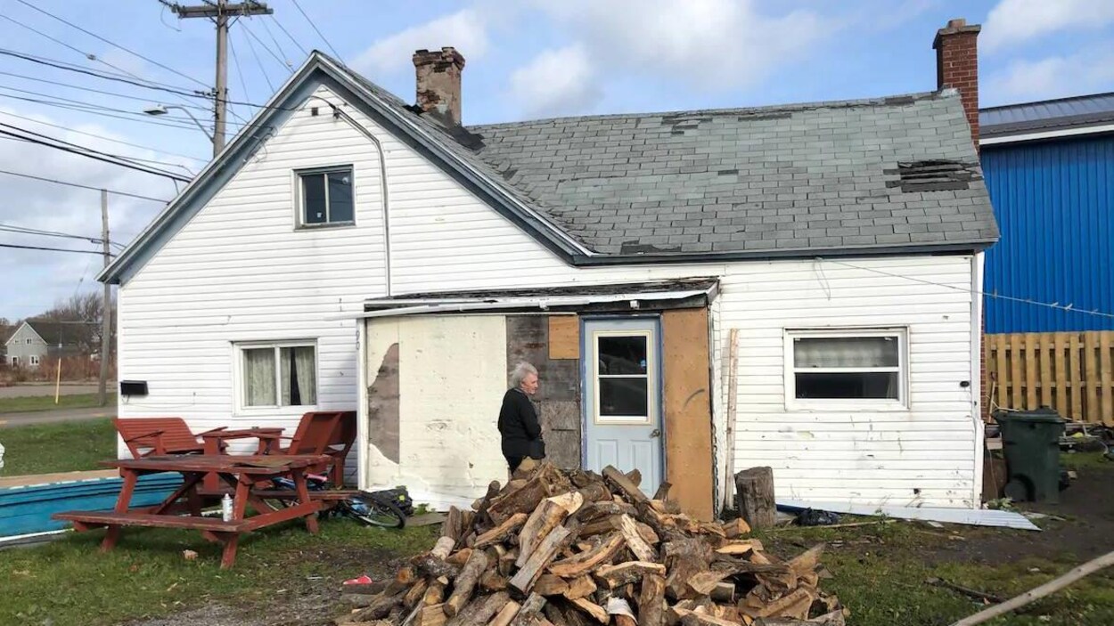 Une dame âgée devant une maison décrépite.