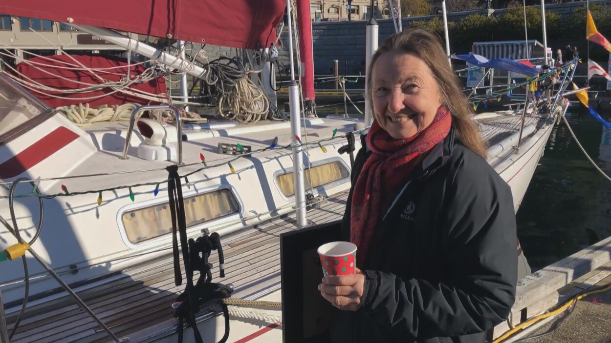 Jeanne Socrates marche sur un quai vers son bateau en portant sous le bras un certificat encadré.