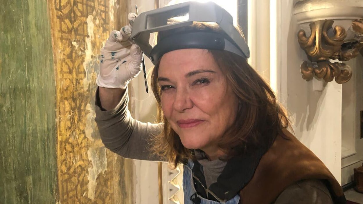 Jennifer Fotheringham, devant la murale, lève les verres grossissants qu'elle porte sur la tête et regarde la caméra.