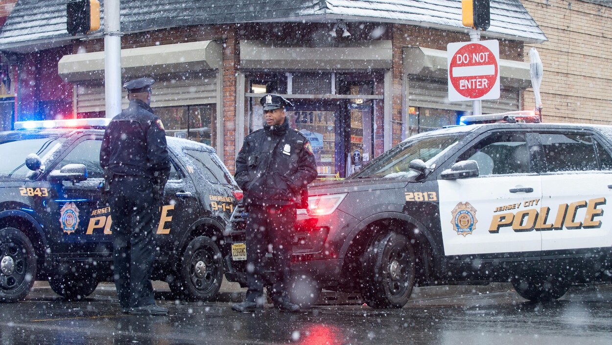 Deux véhicules et des policiers de Jersey City devant une épicerie cacher au coin d'une rue.