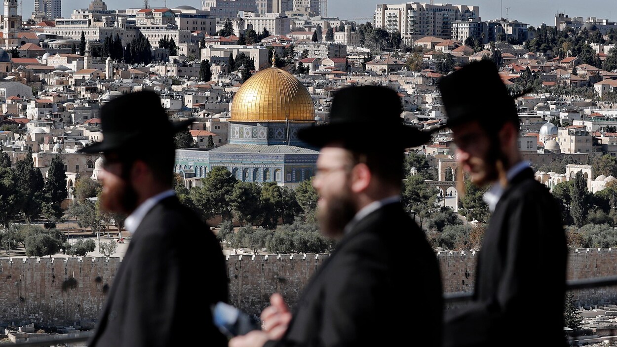 Trois hommes ultra-orthodoxes marchent dans une rue de Jérusalem, avec en arrière-plan le dôme du Rocher.
